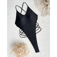Maillot de bain une pièce noir posé à plat sur un tissu blanc, bretelles croisées et lanières sur les côtés