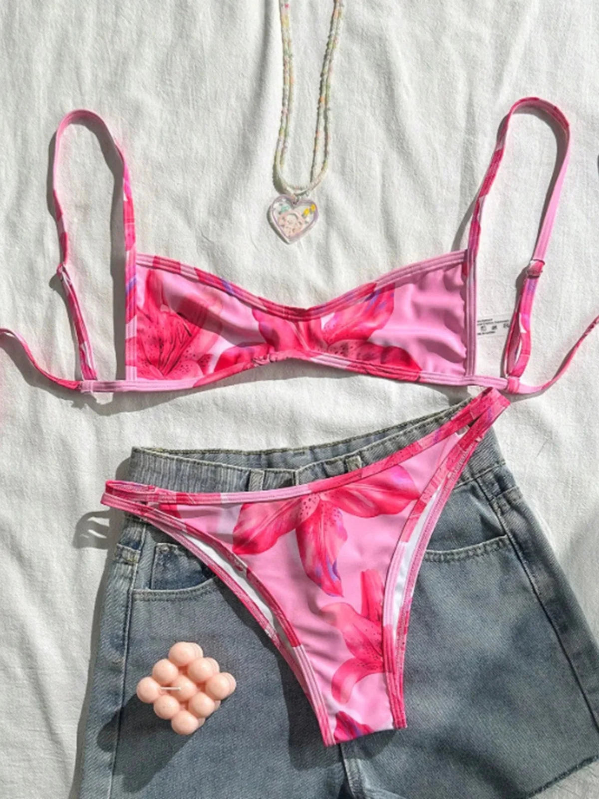 Bikini triangle échancré imprimé fleuri rose posé à plat sur un short en jean, grosses fleurs roses et bretelles fines
