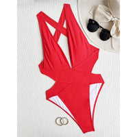 Maillot une pièce rouge décolleté V posé à plat sur tissu blanc, découpe sur les hanches, lunettes de soleil à côté