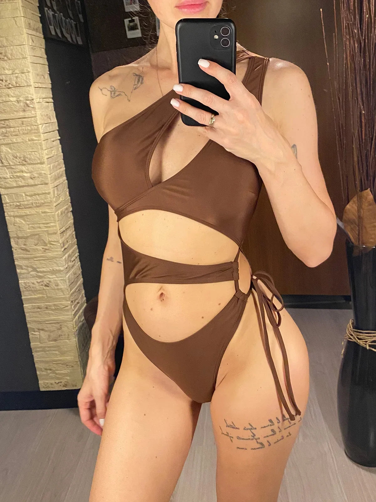 Maillot de bain une pièce asymétrique marron avec anneau doré et lien latéral, porté de face en selfie au miroir