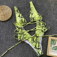 Monokini décolleté plongeant découpe ventre imprimé vert posé à plat sur tapis gris, lanières longues déployées