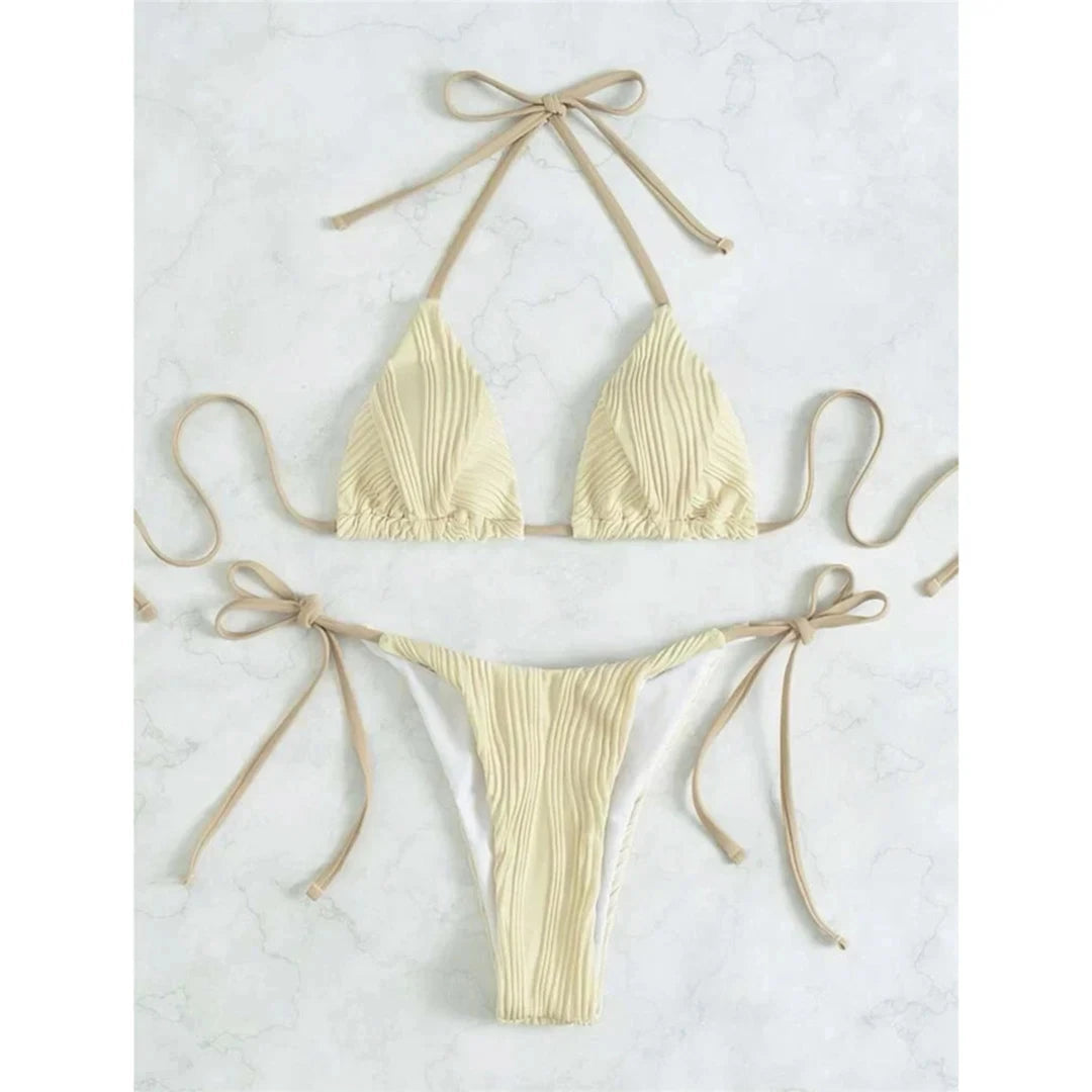 Bikini brésilien tour de cou froncé texturé beige à plat sur du marbre blanc, lacets latéraux longs